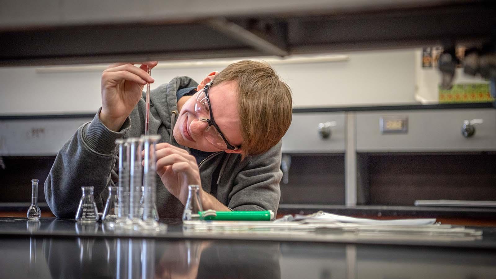 Male student with protective goggles adding chemicals to a beaker